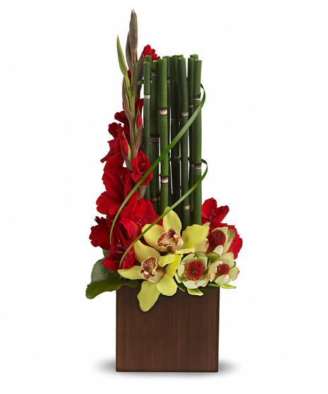 Bamboo stalks, vibrant red gladiolus and delicate green cymbidium orchids arranged in a sleek, dark wooden container.